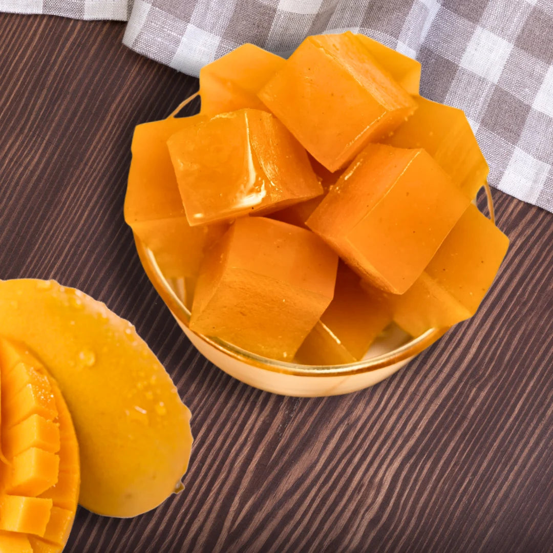 Cubed mango pieces in a glass bowl on a wooden surface with a checkered cloth in the background.