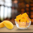 Diced mangoes in a glass bowl on a wooden table with whole mangoes beside it.